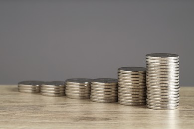 Photo of Stacked coins on wooden table against grey background, closeup with space for text. Salary concept