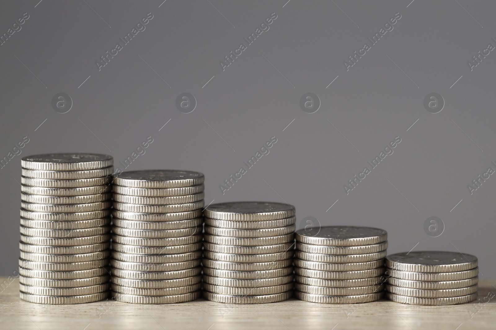 Photo of Stacked coins on wooden table against grey background, closeup with space for text. Salary concept