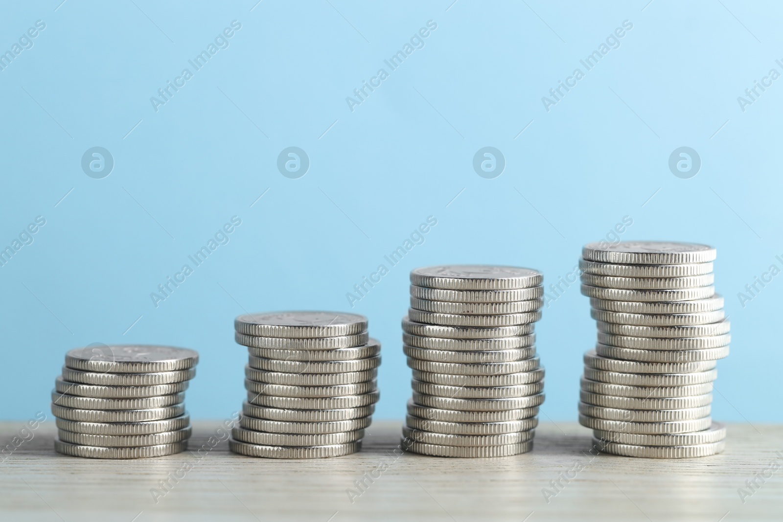 Photo of Stacked coins on wooden table against light blue background, closeup. Salary concept