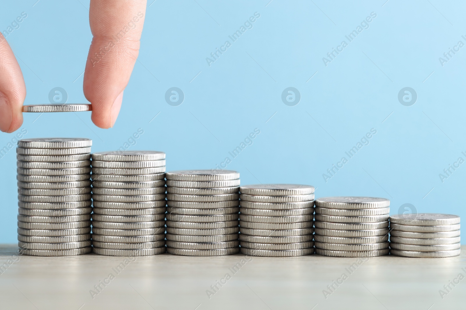 Photo of Woman putting coins at wooden table against light blue background, closeup. Salary concept