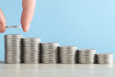 Photo of Woman putting coins at wooden table against light blue background, closeup. Salary concept