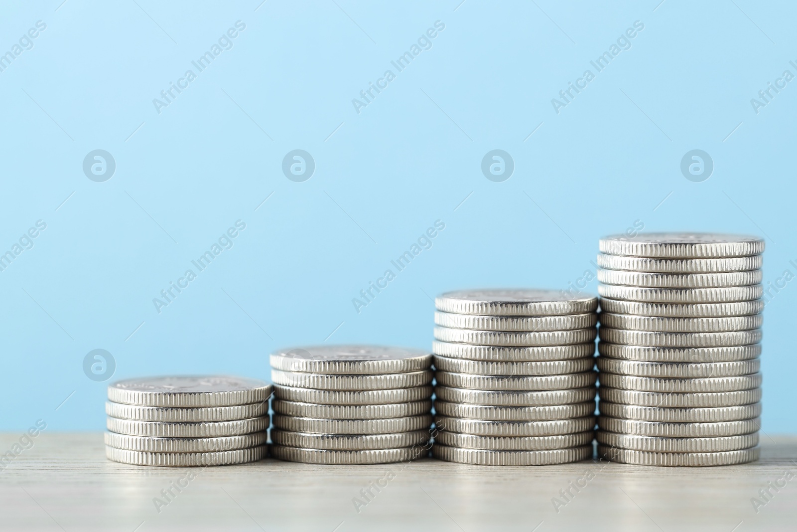 Photo of Stacked coins on wooden table against light blue background, closeup with space for text. Salary concept