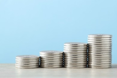 Photo of Stacked coins on wooden table against light blue background, closeup with space for text. Salary concept