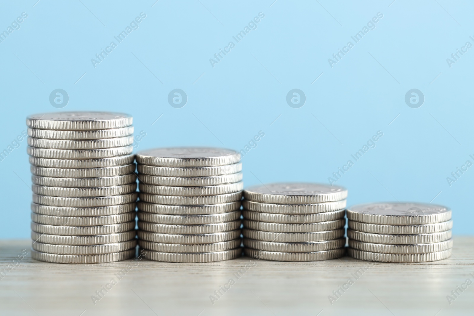 Photo of Stacked coins on wooden table against light blue background, closeup. Salary concept