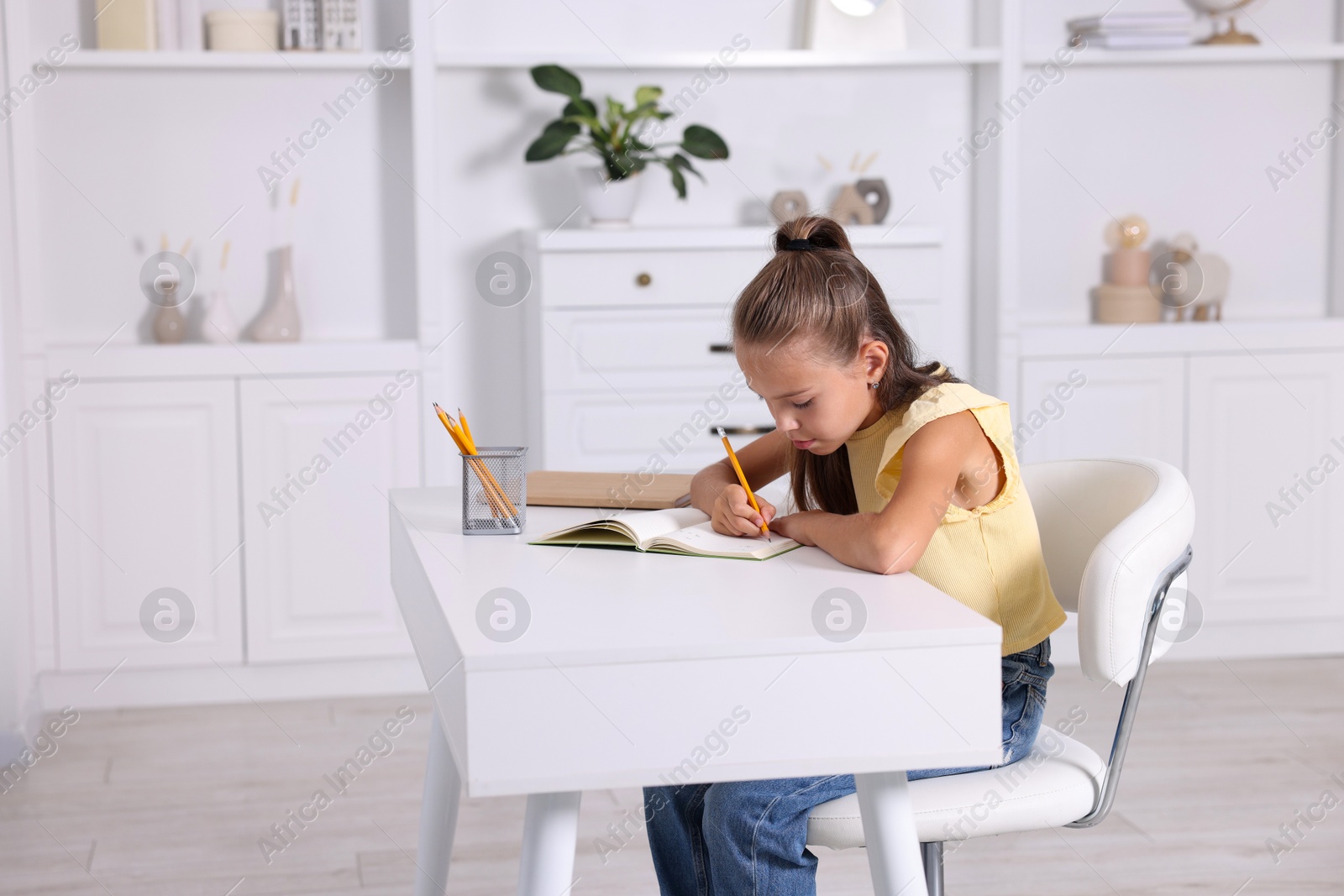 Photo of Girl with incorrect posture doing homework at white desk indoors