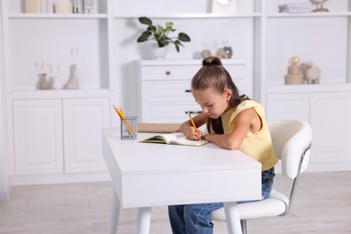 Girl with incorrect posture doing homework at white desk indoors