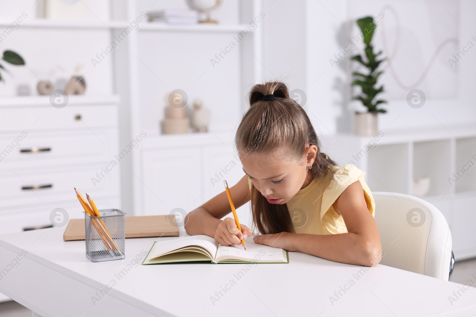 Photo of Girl with incorrect posture doing homework at white desk indoors