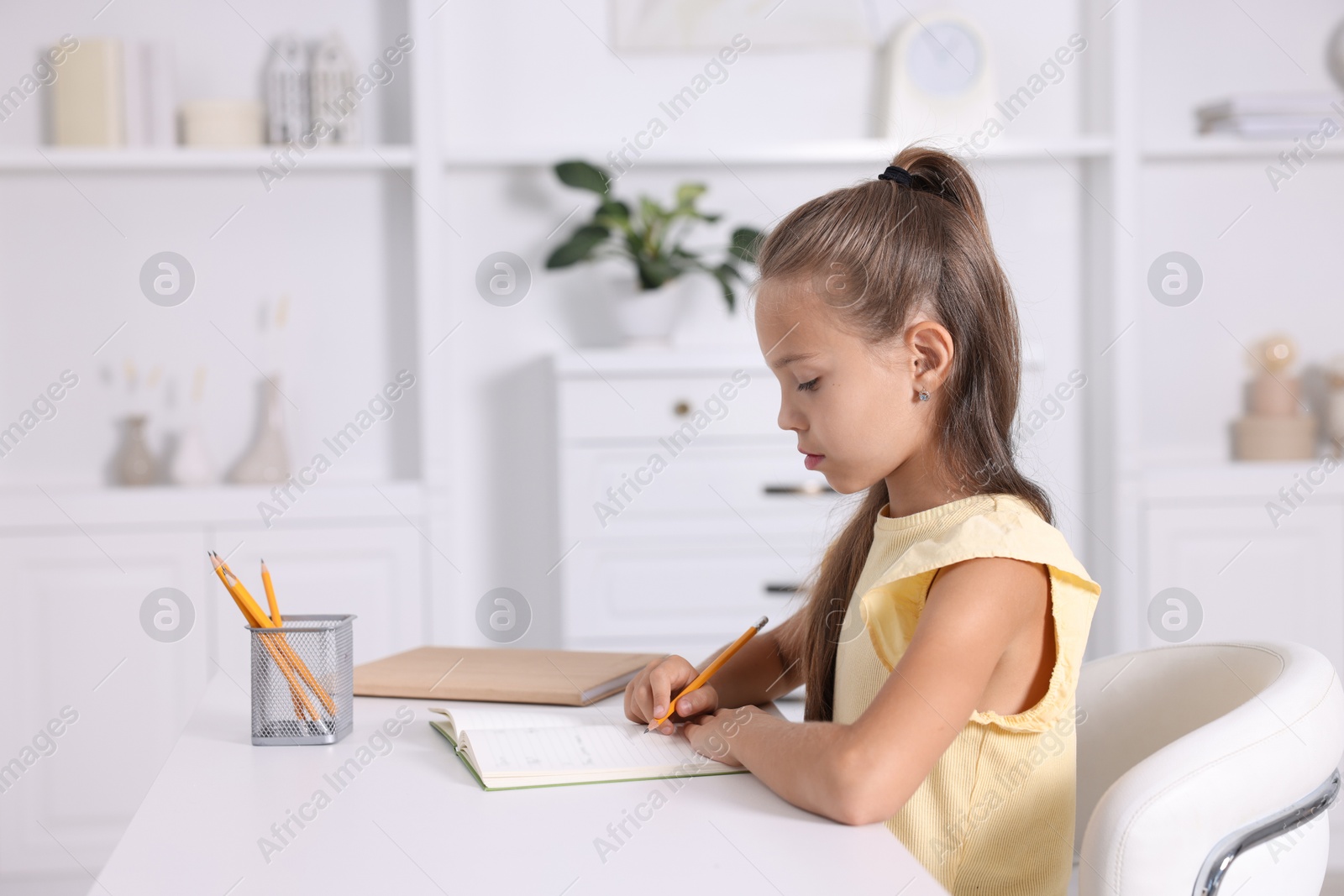 Photo of Girl with correct posture doing homework at white desk indoors