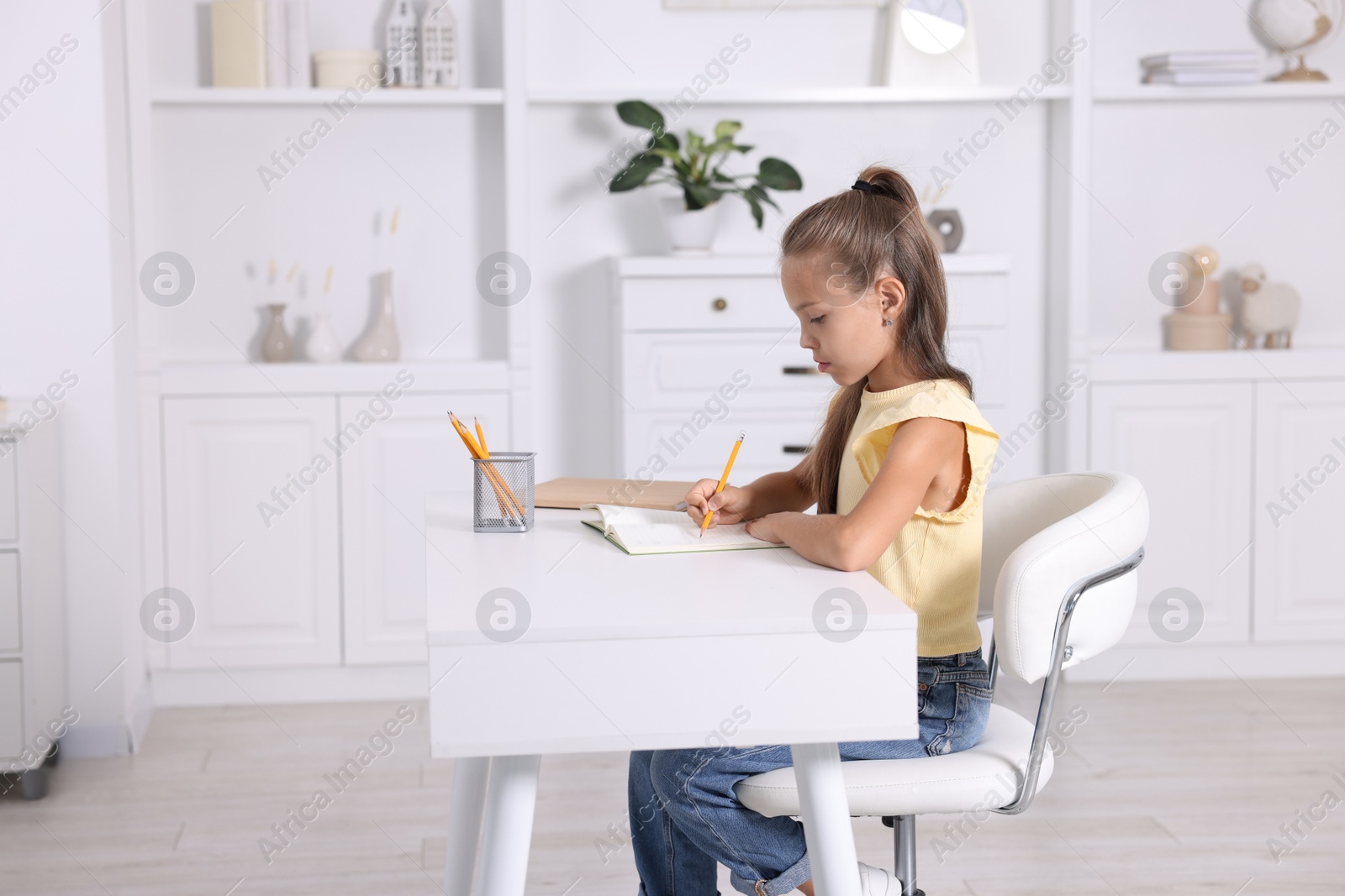 Photo of Girl with correct posture doing homework at white desk indoors