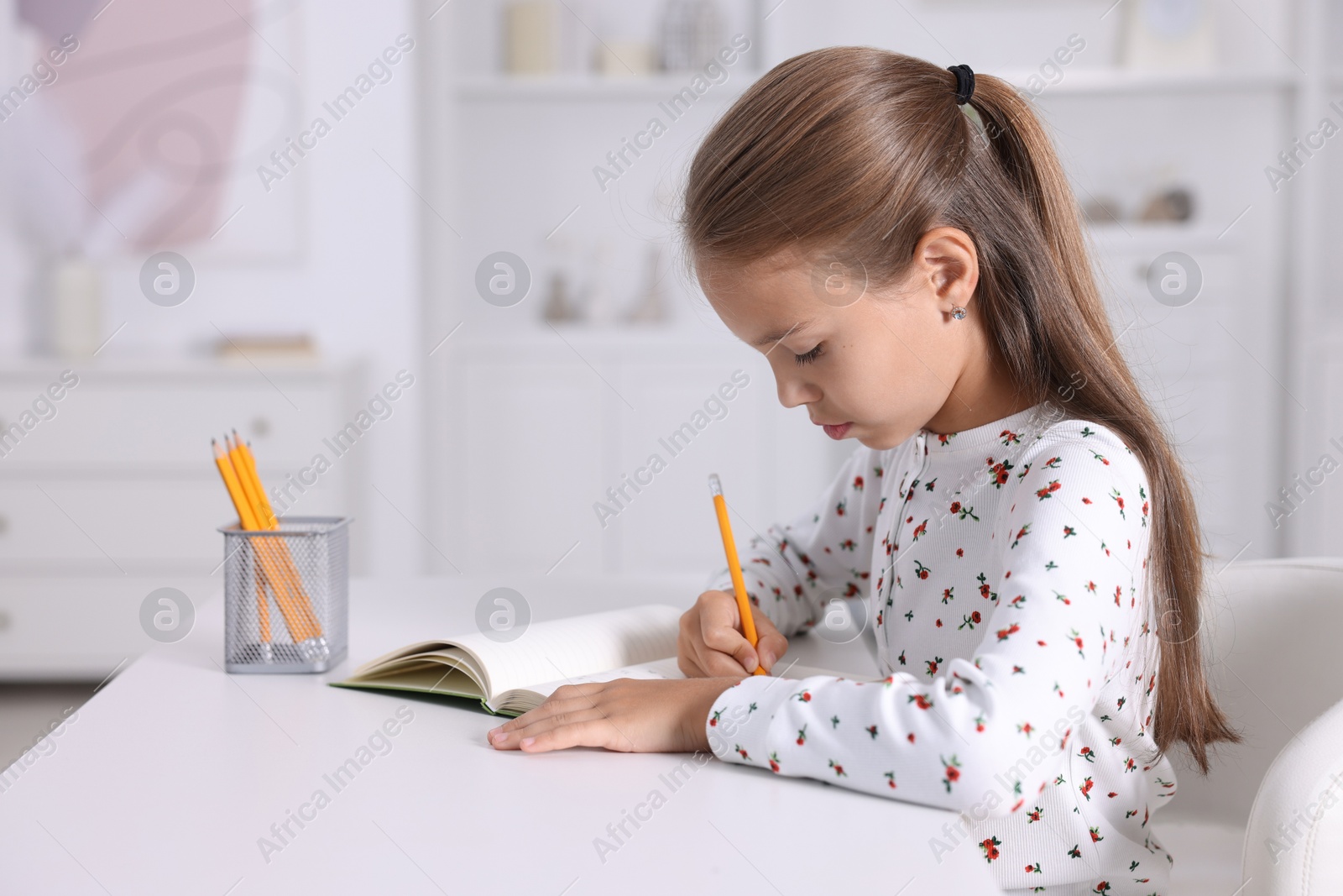 Photo of Girl with correct posture doing homework at white desk indoors