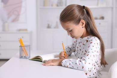 Photo of Girl with correct posture doing homework at white desk indoors