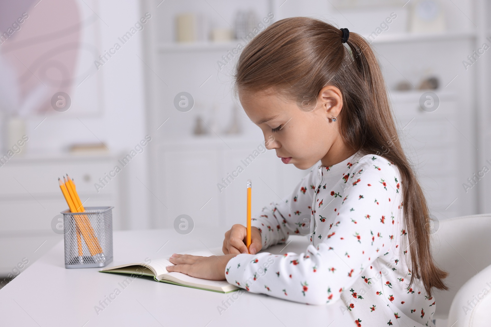 Photo of Girl with correct posture doing homework at white desk indoors