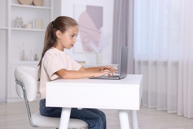 Girl with correct posture using laptop at white desk indoors