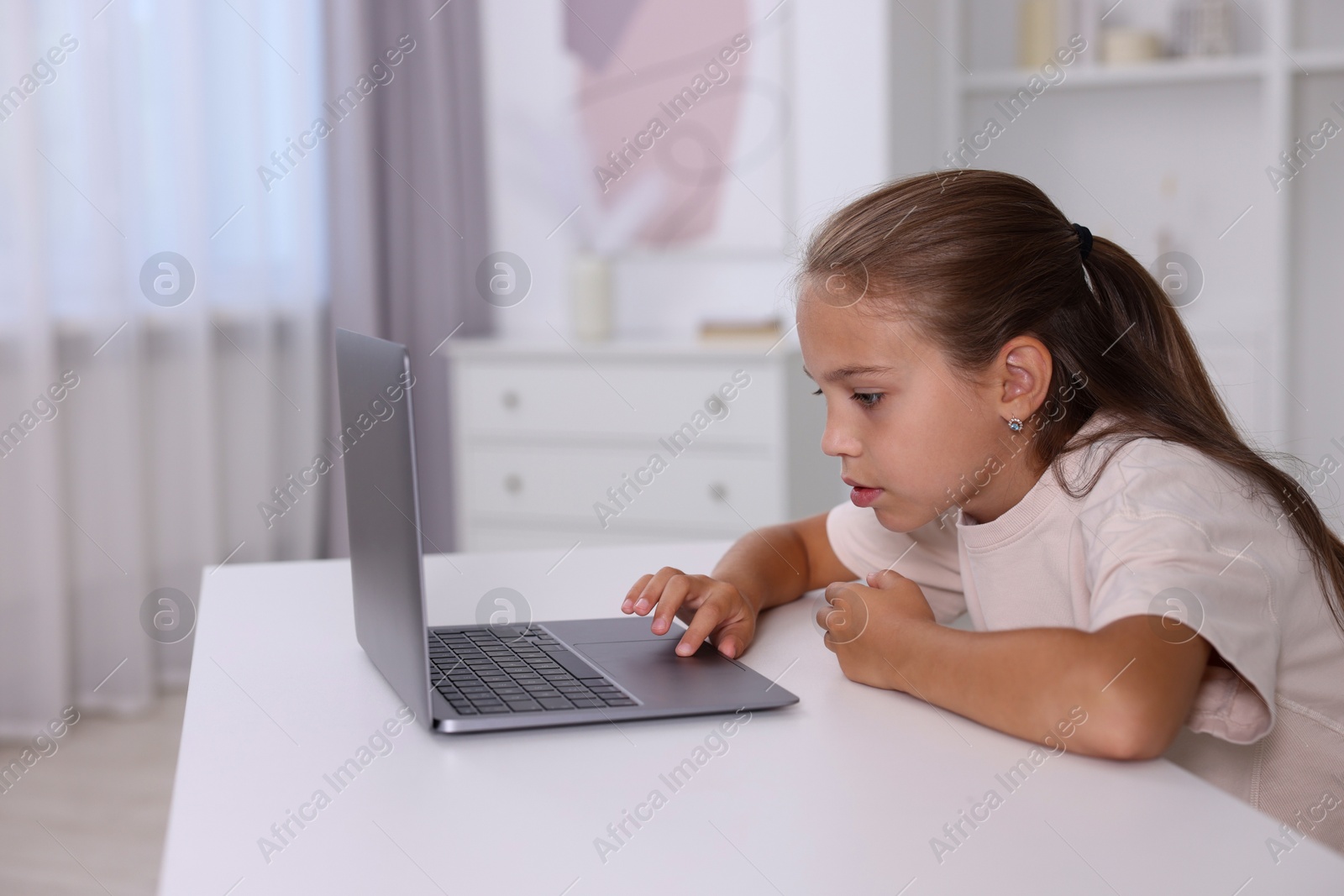 Photo of Girl with incorrect posture using laptop at white desk indoors