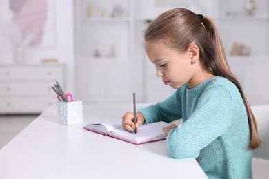 Girl with correct posture doing homework at white desk indoors