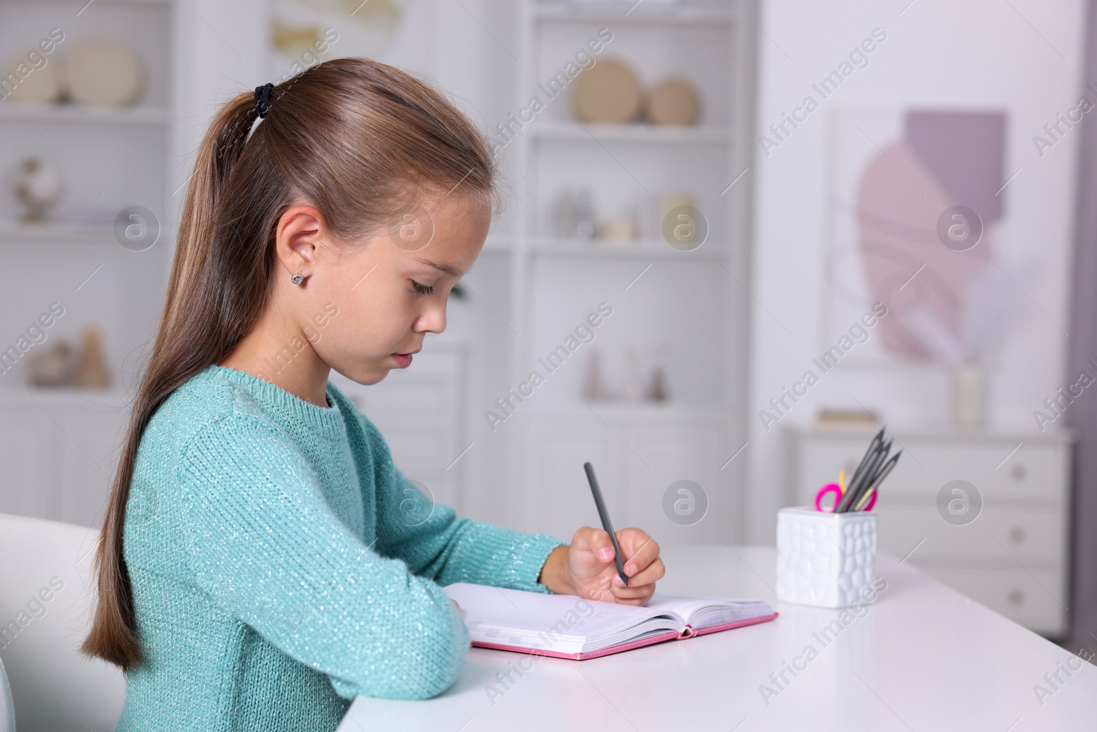 Photo of Girl with correct posture doing homework at white desk indoors