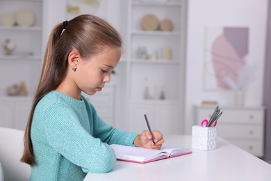 Photo of Girl with correct posture doing homework at white desk indoors