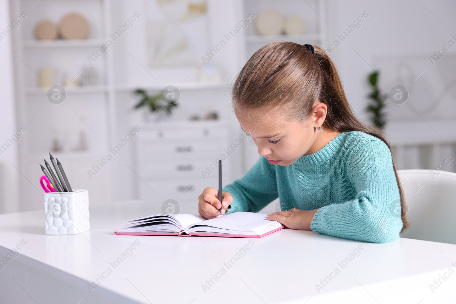 Photo of Girl with incorrect posture doing homework at white desk indoors