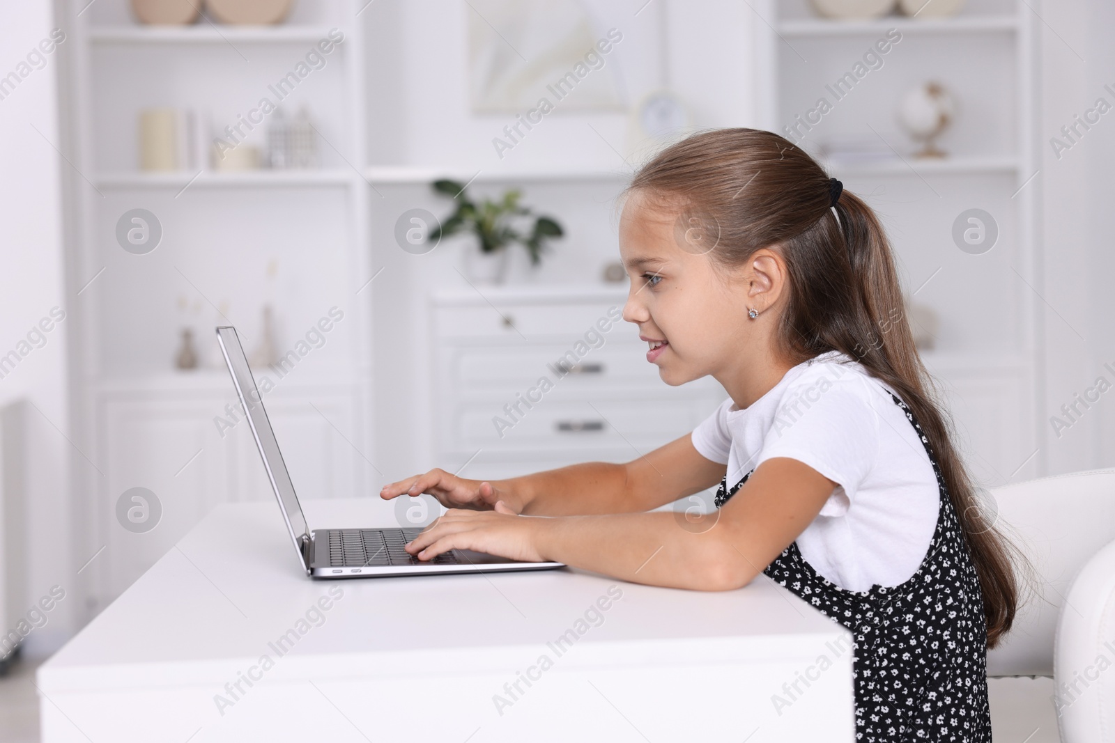 Photo of Girl with incorrect posture using laptop at white desk indoors