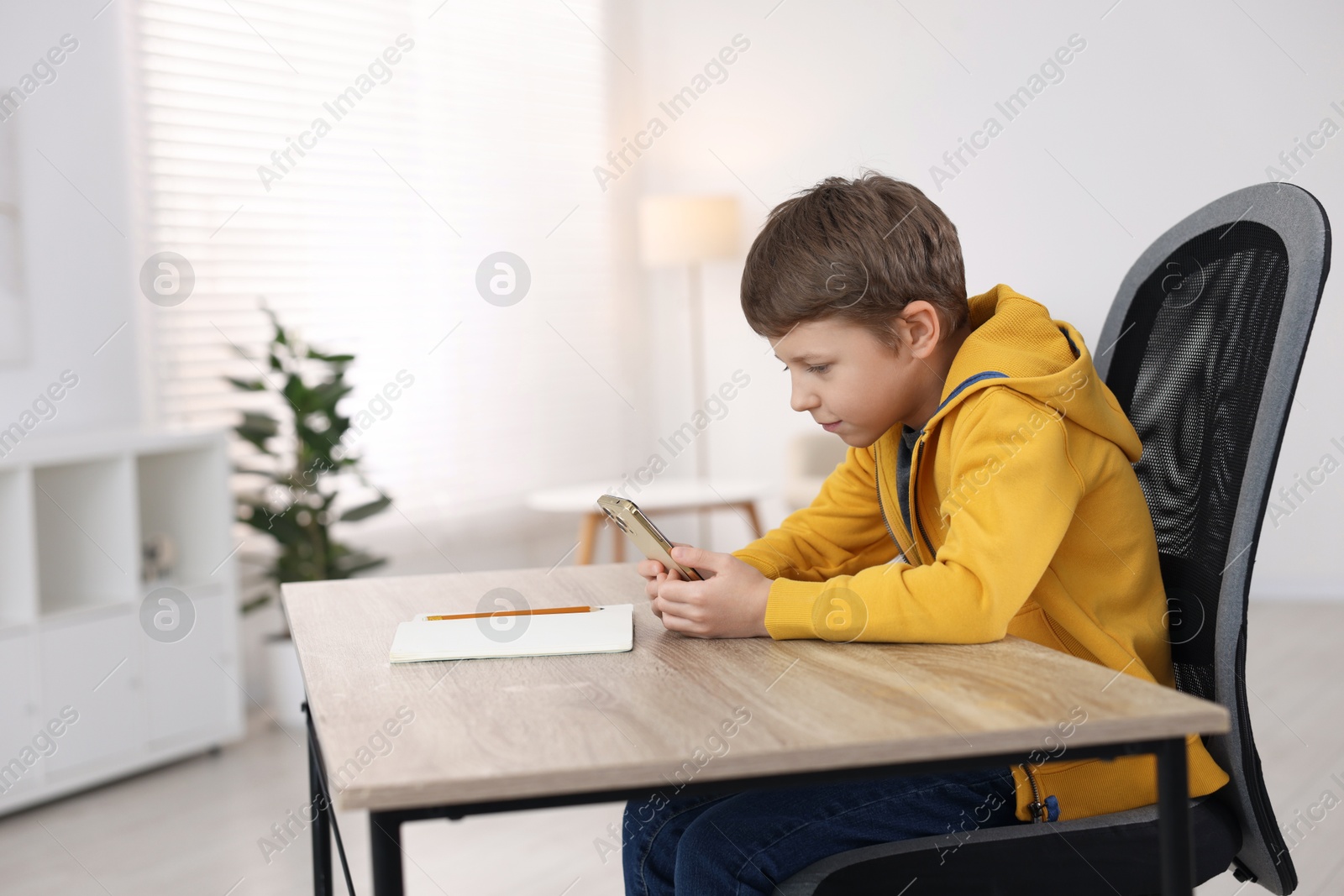 Photo of Boy with incorrect posture using laptop at wooden desk indoors