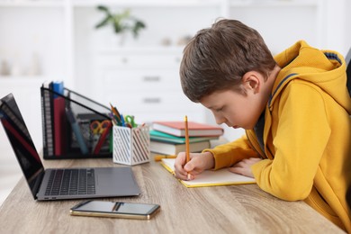 Photo of Boy with incorrect posture using laptop at wooden desk indoors