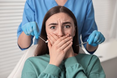 Photo of Dental phobia. Dentist working with scared woman in clinic, closeup