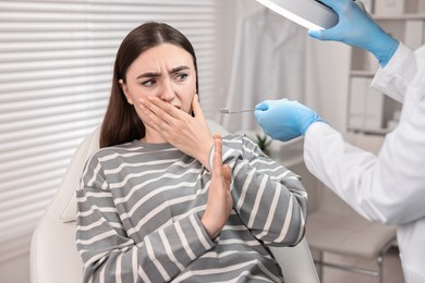 Photo of Dental phobia. Dentist working with scared woman in clinic, closeup