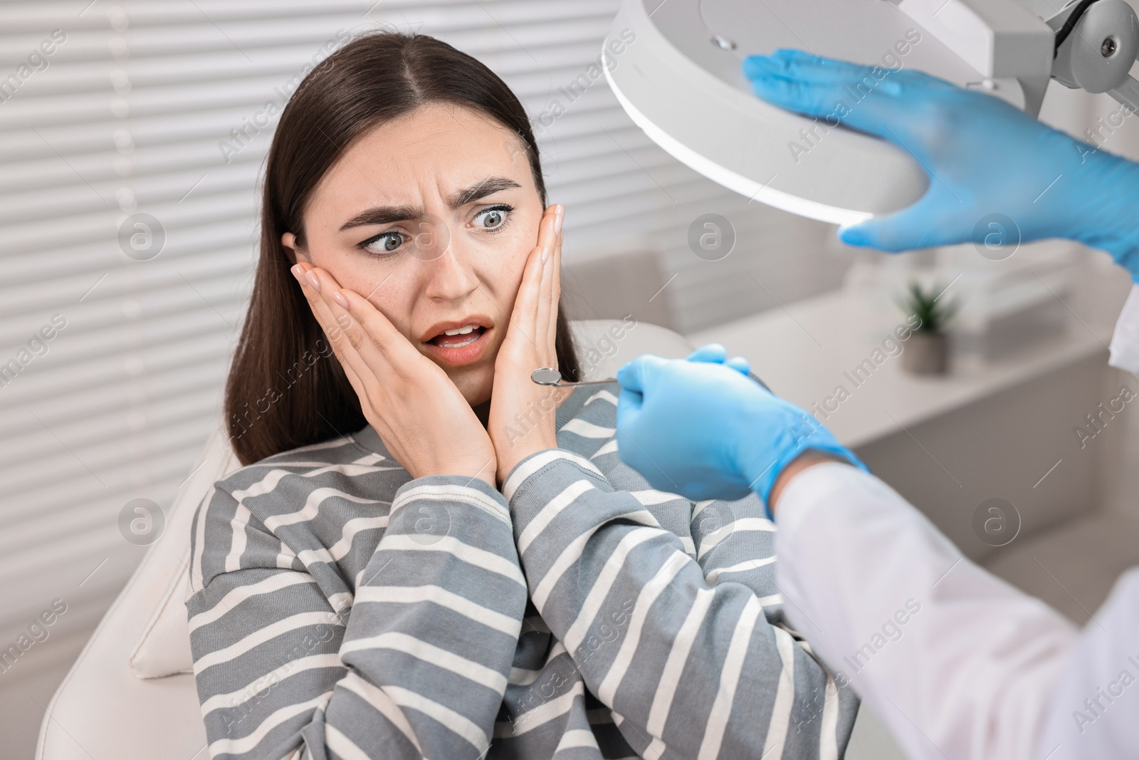 Photo of Dental phobia. Dentist working with scared woman in clinic, closeup