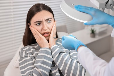 Photo of Dental phobia. Dentist working with scared woman in clinic, closeup