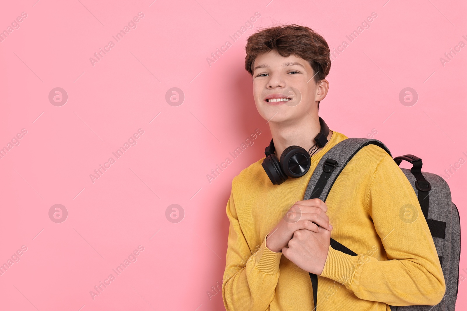 Photo of Happy teenage boy with headphones and backpack on pink background, space for text