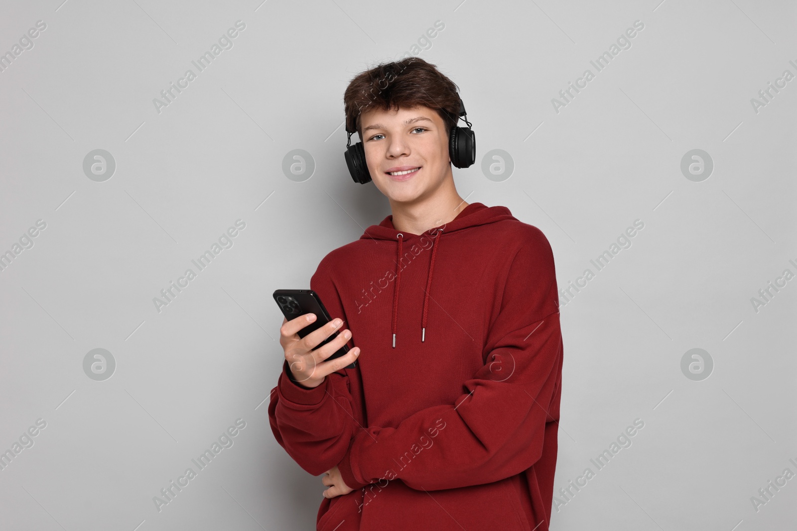 Photo of Teenage boy in headphones with smartphone on light grey background, space for text