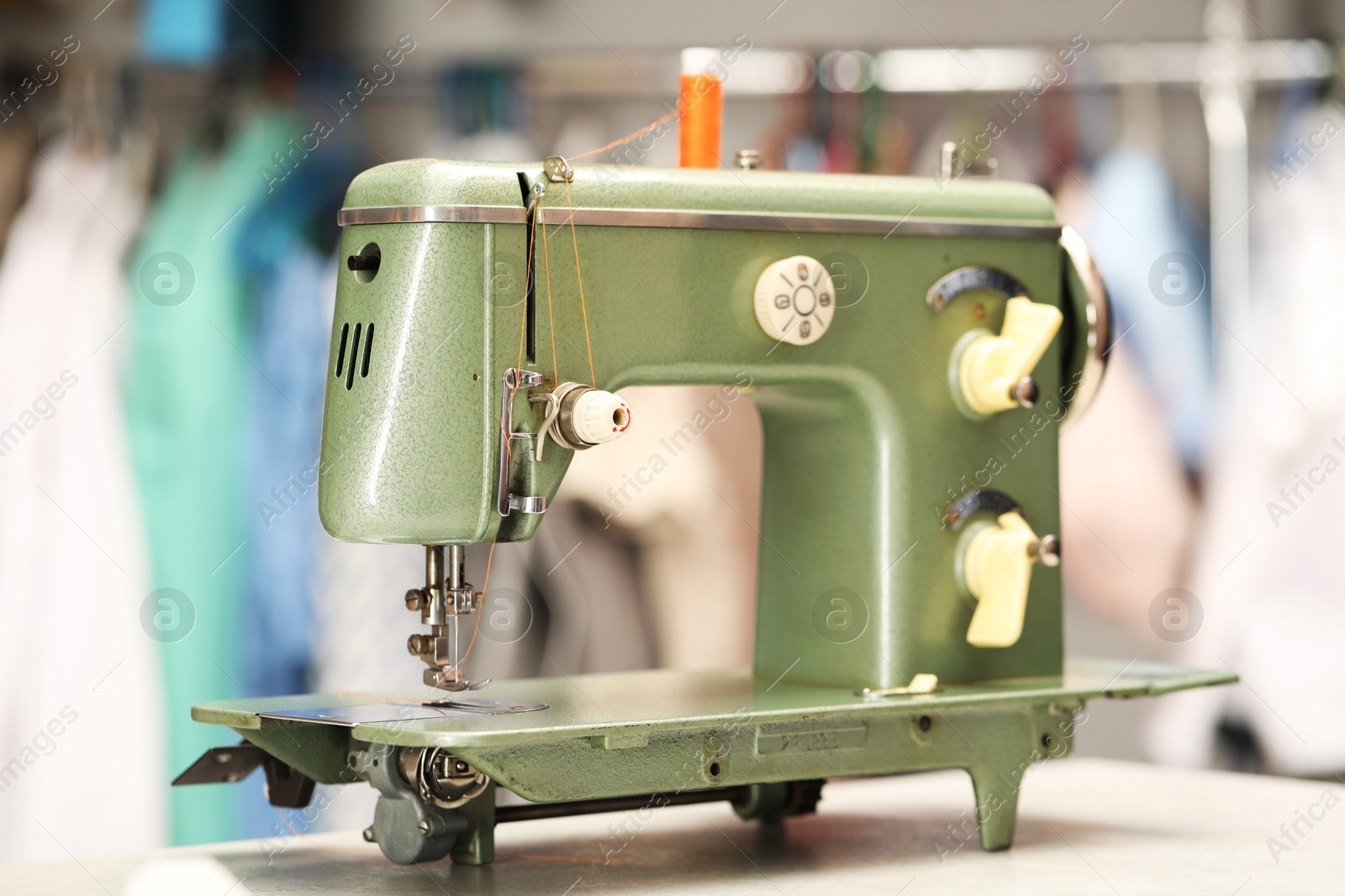 Photo of Vintage sewing machine with thread on white table in workshop, closeup