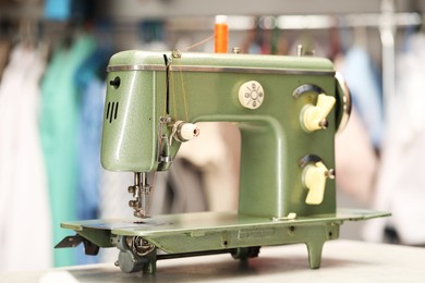 Photo of Vintage sewing machine with thread on white table in workshop, closeup