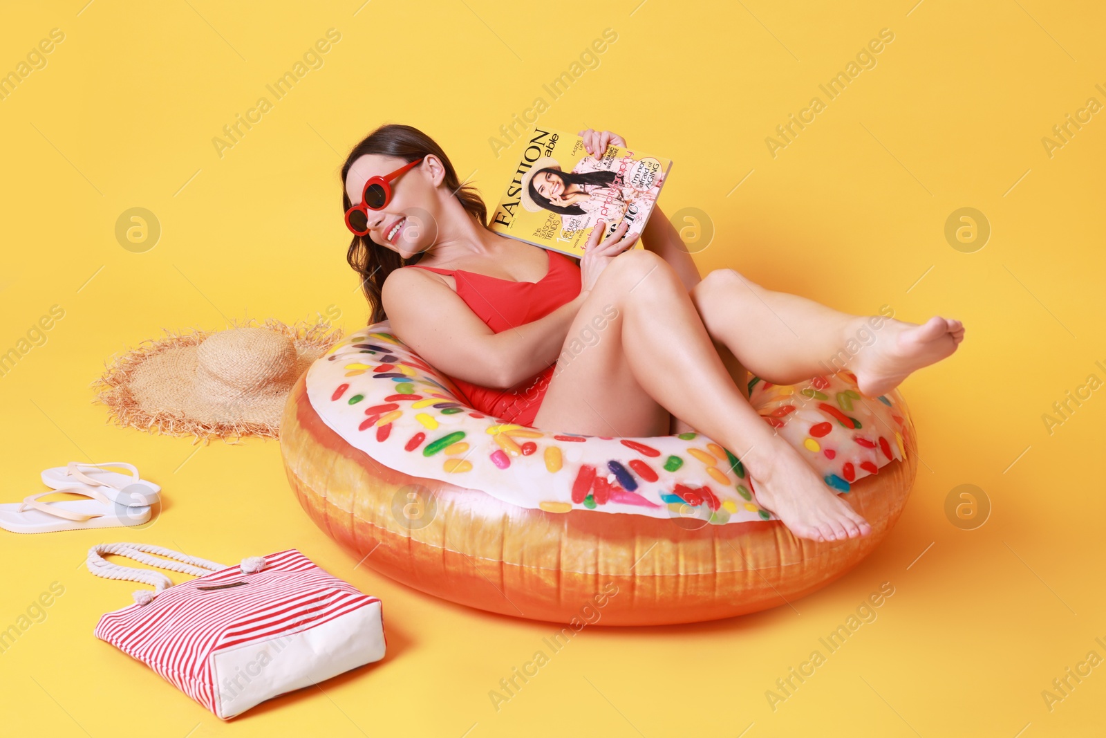 Photo of Beautiful woman with beach accessories reading magazine on yellow background