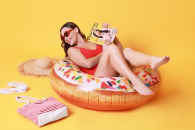 Photo of Beautiful woman with beach accessories reading magazine on yellow background