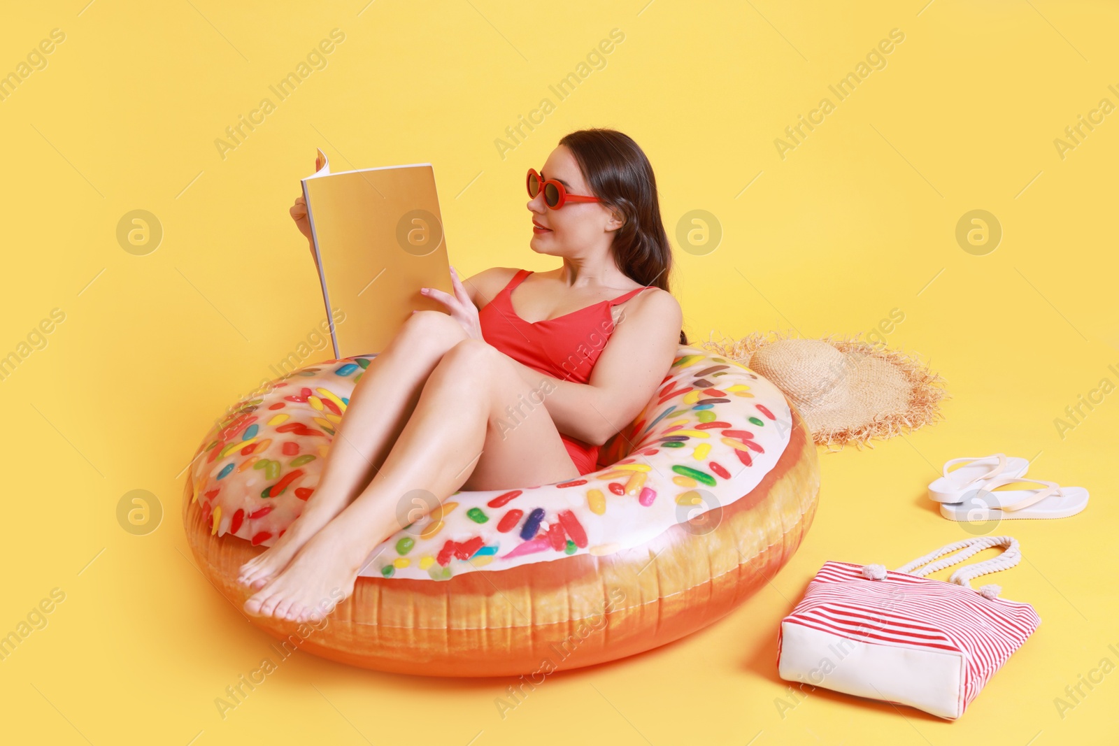 Photo of Beautiful woman with beach accessories reading magazine on yellow background