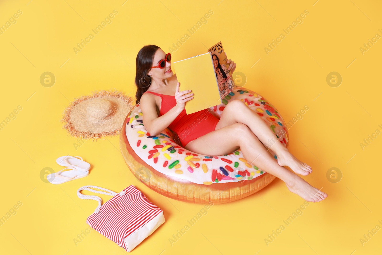 Photo of Beautiful woman with beach accessories reading magazine on yellow background