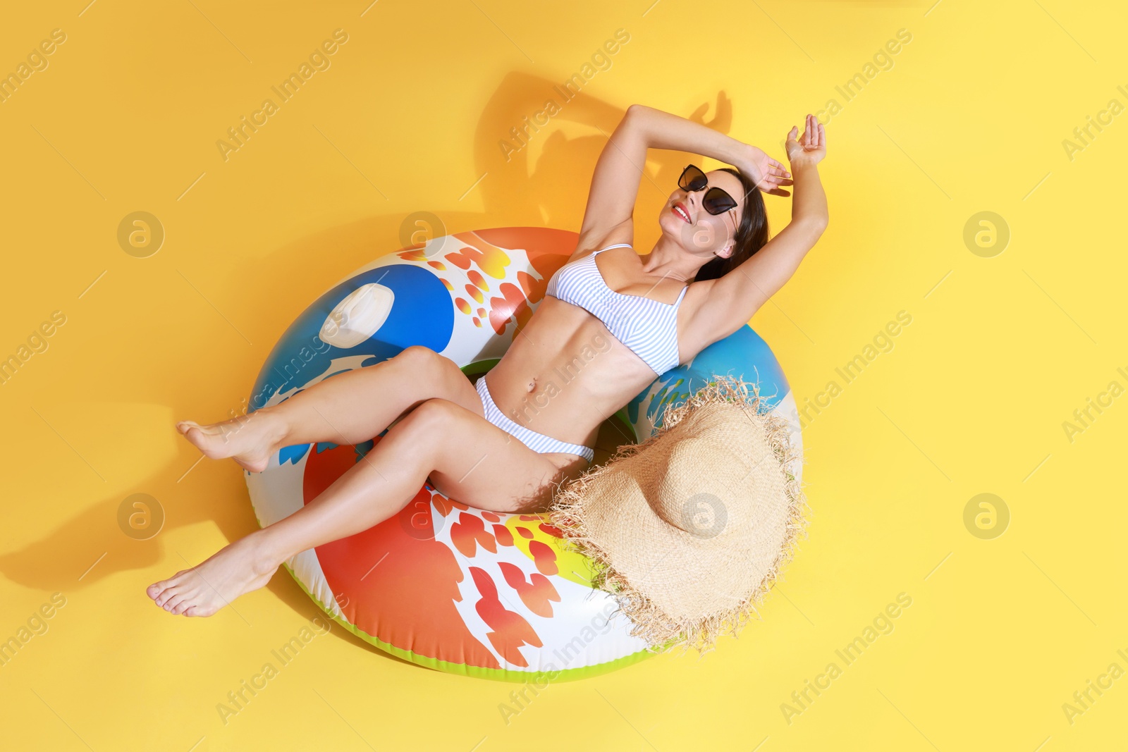 Photo of Beautiful woman in swimsuit with inflatable ring on yellow background