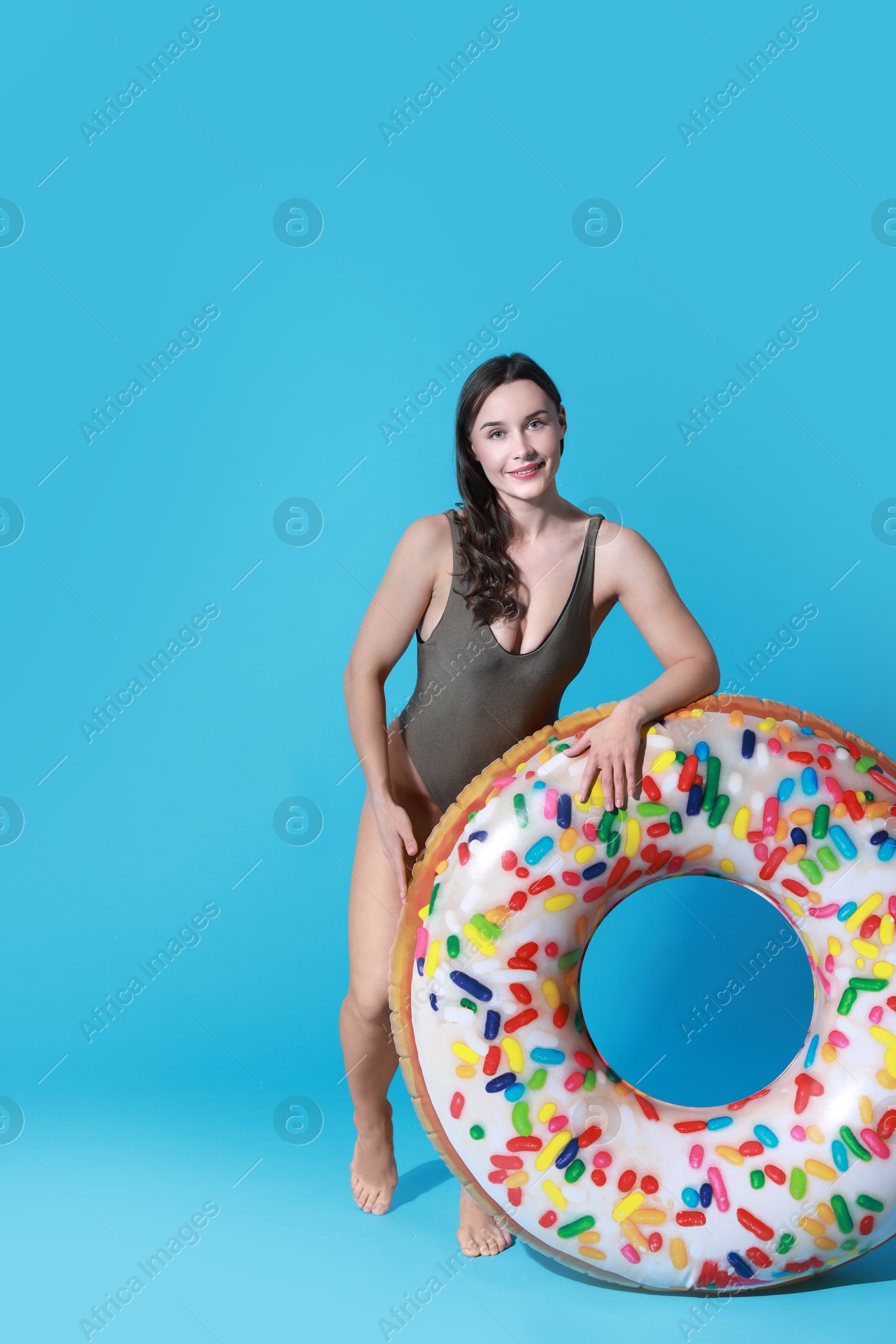 Photo of Beautiful woman in swimsuit with inflatable ring on light blue background