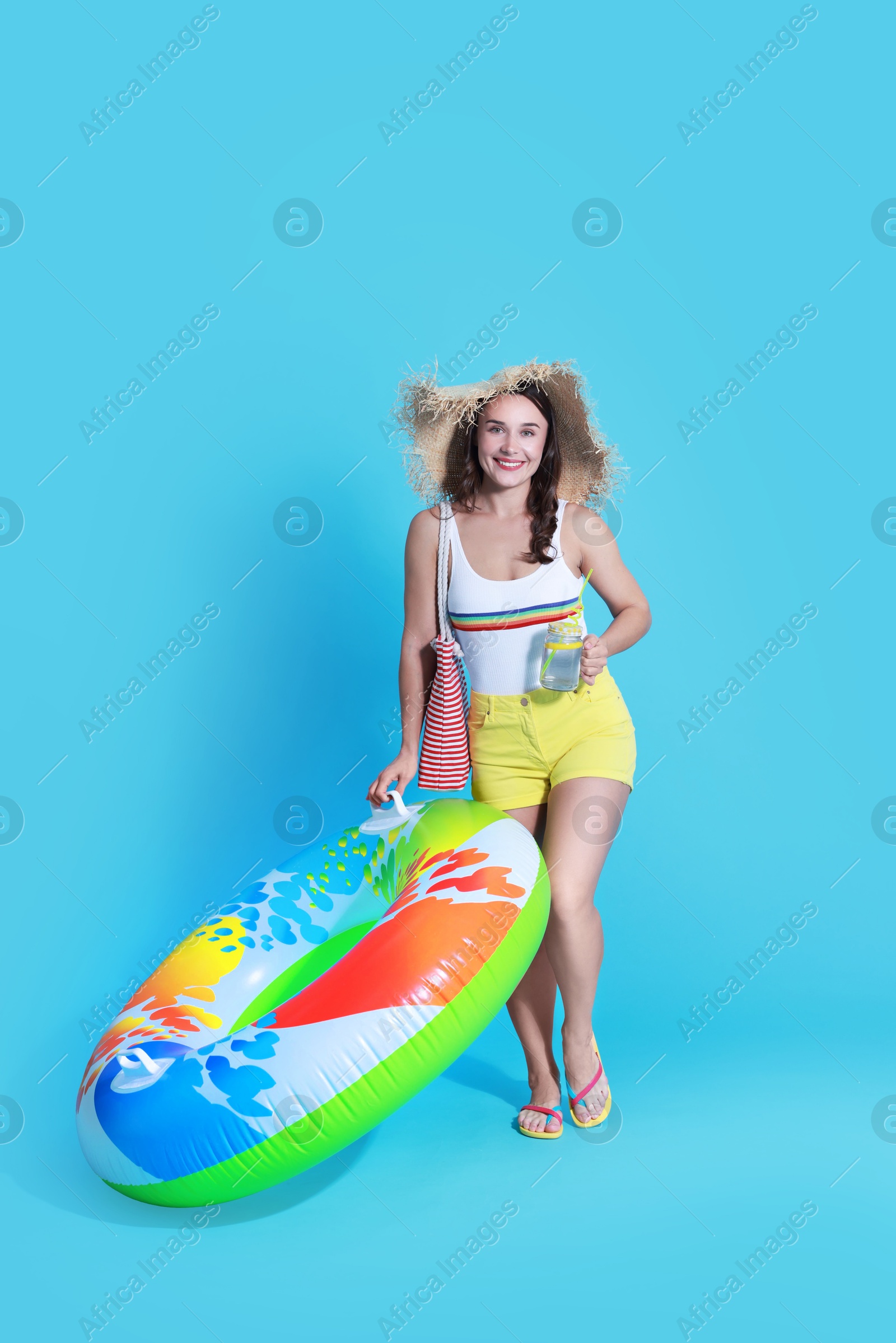 Photo of Beautiful woman in swimsuit with inflatable ring and drink on light blue background