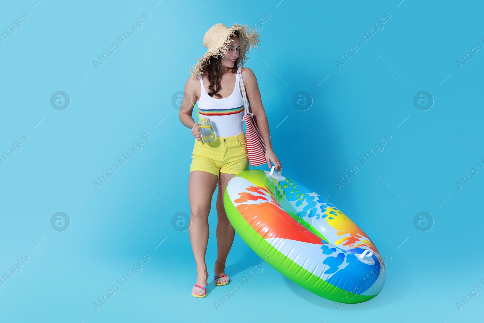 Photo of Beautiful woman in swimsuit with inflatable ring and drink on light blue background