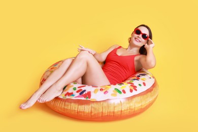 Photo of Beautiful woman in swimsuit with inflatable ring on yellow background