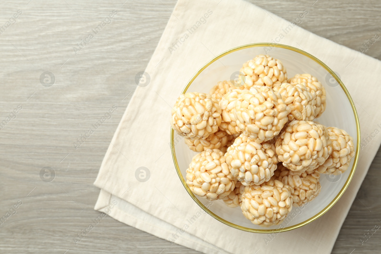 Photo of Tasty puffed rice balls in bowl on wooden table, top view. Space for text