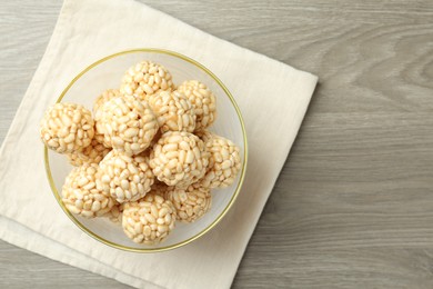 Tasty puffed rice balls in bowl on wooden table, top view. Space for text