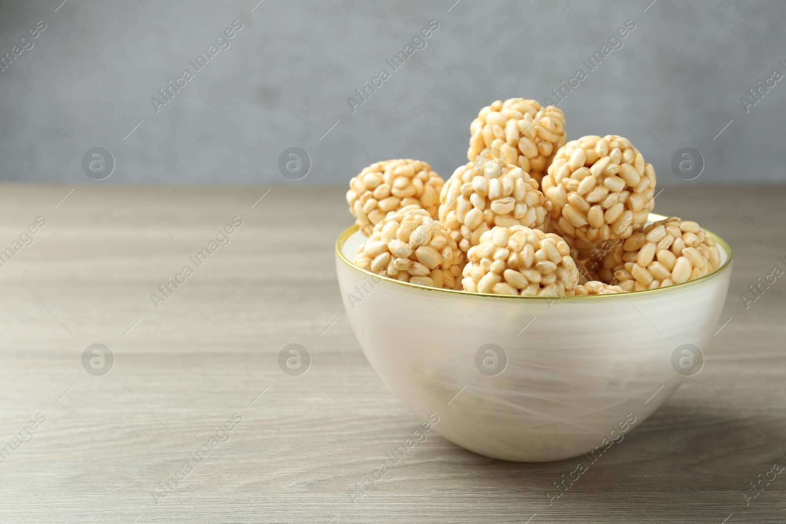 Photo of Tasty puffed rice balls in bowl on wooden table, closeup. Space for text