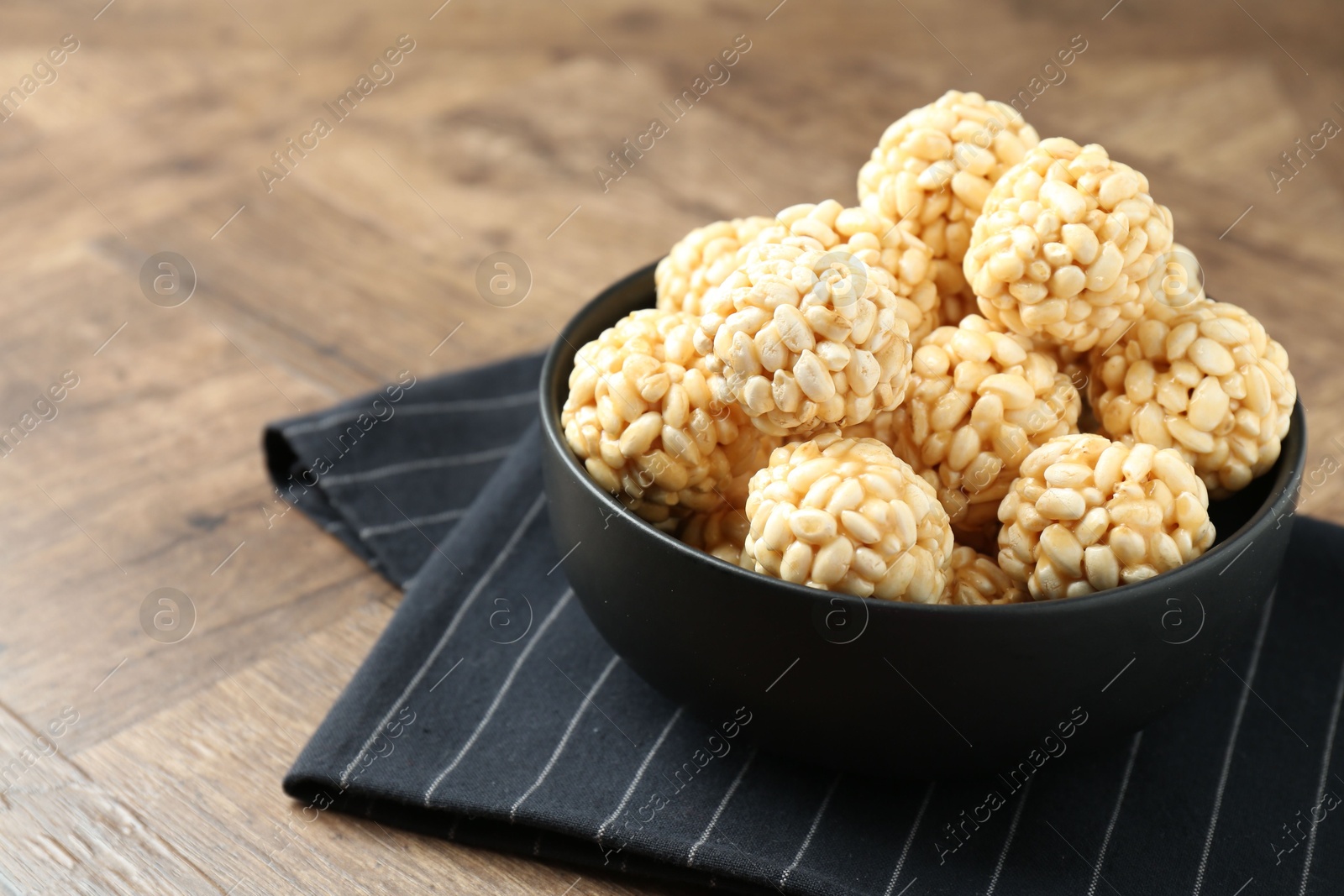 Photo of Tasty puffed rice balls in bowl on wooden table, closeup. Space for text