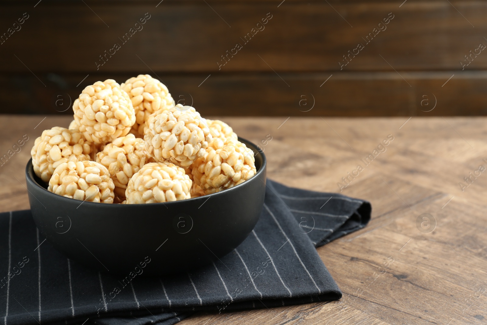 Photo of Tasty puffed rice balls in bowl on wooden table, closeup. Space for text