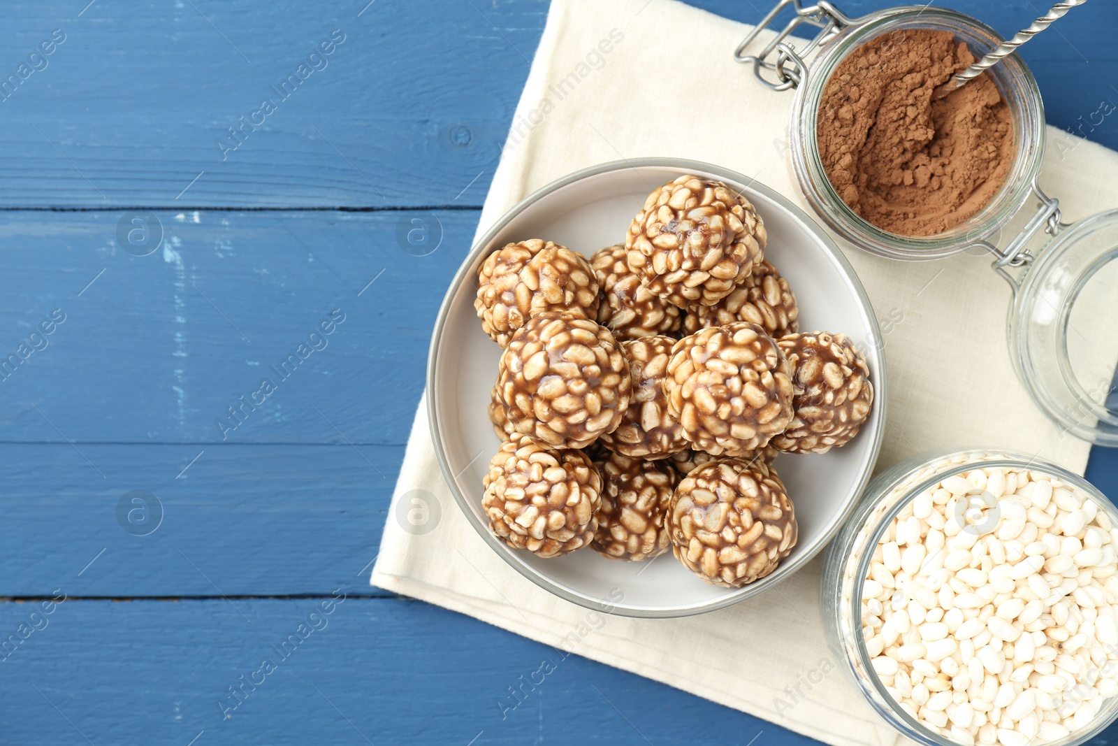 Photo of Tasty chocolate puffed rice balls and ingredients on blue wooden table, flat lay. Space for text