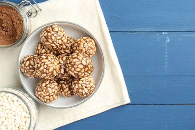 Tasty chocolate puffed rice balls and ingredients on blue wooden table, flat lay. Space for text