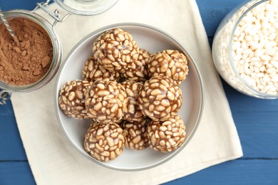 Tasty chocolate puffed rice balls and ingredients on blue wooden table, flat lay